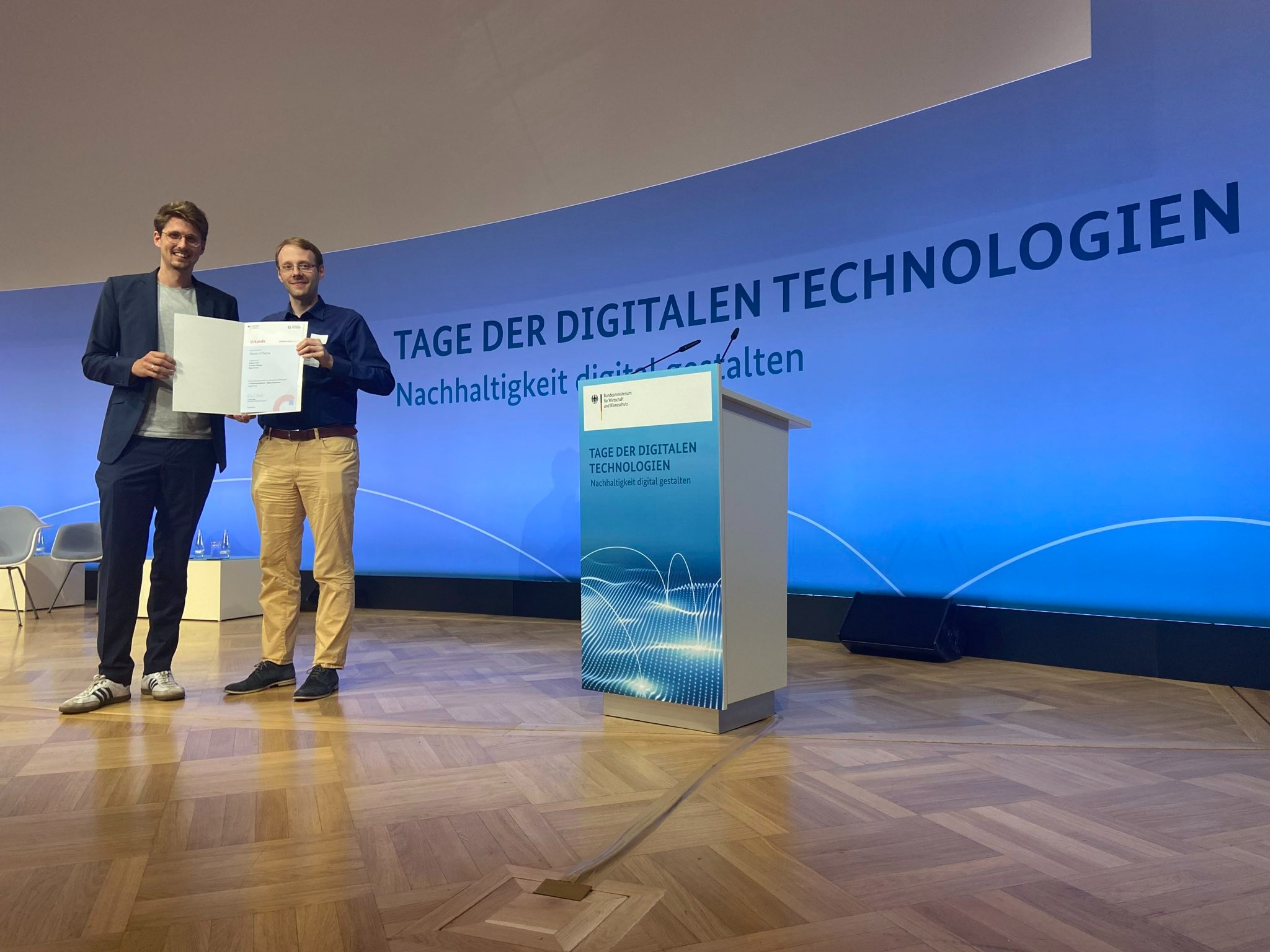 Moritz Oberberg und Geoffrey Mellar auf der Bühne der Veranstaltung "Tage der digitalen Technologien" mit der Urkunde zum Gründungspreis